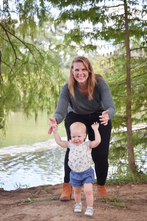 Mother holds hand of young child as she learns to walk